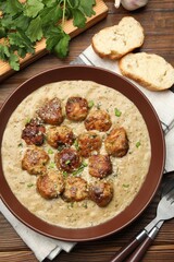 Delicious meatballs with gravy cream sauce and herbs served on wooden table, flat lay