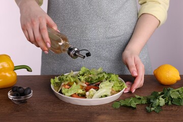 Woman pouring oil onto tasty salad at wooden table against white background, closeup