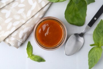 Tasty curry sauce in glass jar and basil on white tiled table, flat lay