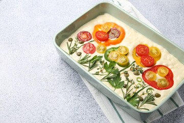 Raw focaccia with vegetables and spices in baking dish on light grey table, closeup. Space for text