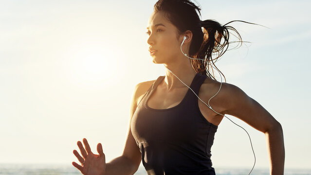 Exercise, running and woman on beach with earphones, sunrise and commitment to healthy outdoor workout. Music, training and girl at ocean for morning fitness, body wellness and jogging in nature.