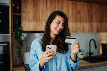 Fototapeta premium Young caucasian woman shop or pay online using credit card and cellphone
