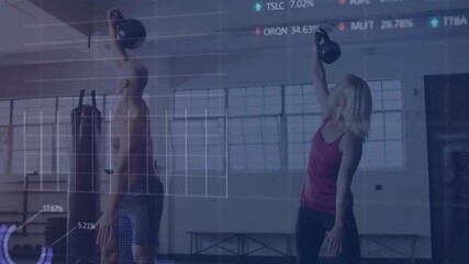 Mid adult man and woman lifting kettlebells in gym studio, displaying finance charts overlaying - Powered by Adobe