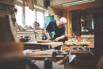 A senior handyman working in his home garage or workshop cutting or sanding wood. Skilled mature...