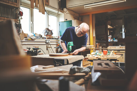 A senior handyman working in his home garage or workshop cutting or sanding wood. Skilled mature male craftsman building, repairing or cutting a piece of wood in his woodwork shop