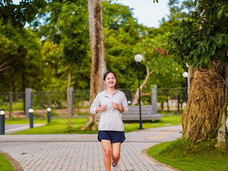 Asian fitness woman jogging in the park, enjoying self care, using smartwatch for data tracking. mental healthcare. Southeast Asian wellness lifestyle and exercise. People running focus weight loss