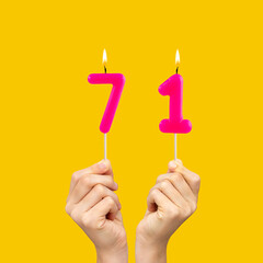Hands holding birthday candles with number 71 - Yellow background
