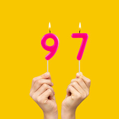 Hands holding birthday candles with number 97 - Yellow background