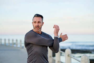 Fitness, mature man and stretching by beach for workout preparation, getting ready and muscle recovery. Space, arms warm up and training at promenade for wellness challenge and exercise performance