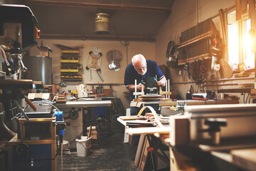 Working mature senior carpenter building, planning and making furniture indoors in a workshop. Elderly man work, make and design a wood chair. Old male holding and using tools for a retirement hobby