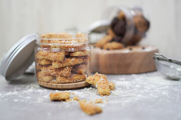 an open jar filled with cheese cookies on wooden coaster and some cookies outside, with cookie jar open and lying on a wooden pedestal in the background