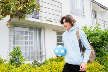 Student walking home from school carrying soccer ball and backpack