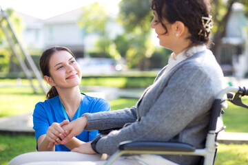 Young caucasian nurse comforting with patient while sitting on wheelchair in outdoor park, doctor woman support and counseling with patient, caregiver and service, medical and consoling.