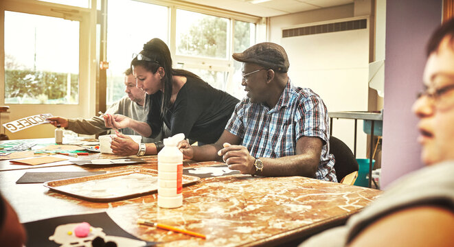 Artistic, creative people with learning disabilities in class at a community center. A black woman is teaching the group while the adults learn, listen and enjoy arts and crafts together.