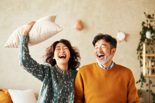 Happy Asian couple laughing together in a cozy bedroom, sharing a joyful and authentic moment of connection and emotion. - Powered by Adobe