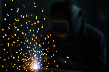 Welder wearing protective gear working with bright sparks and detailed focus in dim workshop
