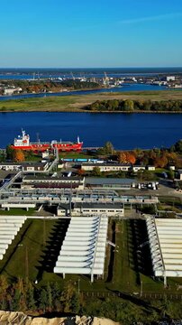 Vertical drone shot of a cruise ship docked at a port along a wide river during daytime.