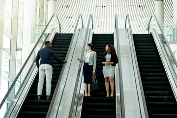 Office, walking and business people on escalator in lobby for meeting, discussion and networking. Professional, corporate and men and women at conference, convention and seminar in modern building
