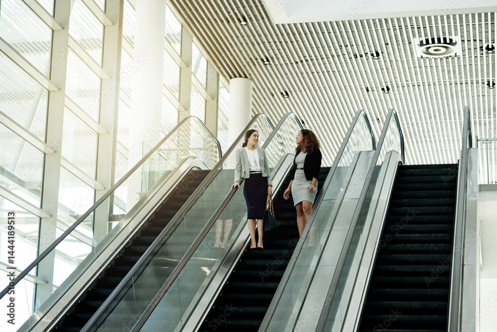 Poster office, escalator and business women in conversation in lobby for meeting, discussion and networking