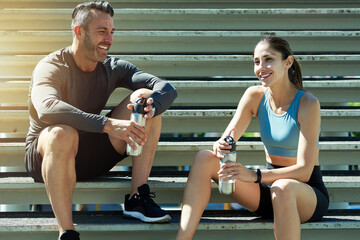 Naklejka premium Talking, fitness and couple on break, steps and happy for exercise in morning, summer and healthy. Outdoor, rest and people with sportswear for workout, training and smile with routine for wellness