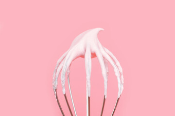 Whisk with whipped cream from proteins close-up on pink background.