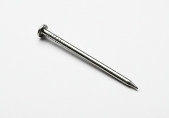 A single metal nail with a flat head and a pointed tip lying on a white surface in a close up view