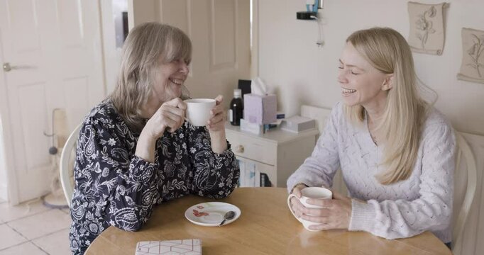 Kitchen, coffee and women happy together communication bonding at home. Happiness support, mother smile and woman laugh fun conversation drink warm tea, family love and people discuss life indoors