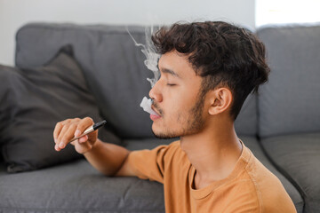 Man smoking with an e-cigarette blowing smoke from mouth, and enjoying leisure time indoors