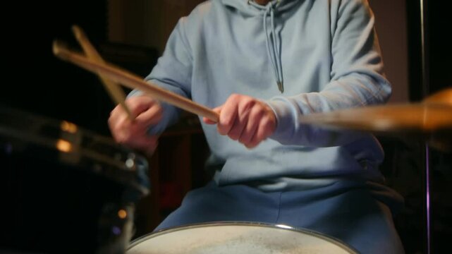 Drummer passionately plays drum set with dynamic stick movements, showcasing rhythmic skills and musical energy. Close-up captures intense focus and physicality of live percussion performance.