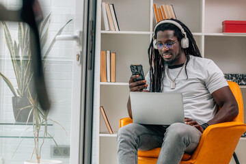 young african man with headphones, mobile phone and computer listening to music at home