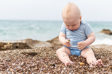 Little baby boy sitting on beach pebbles. Happy little baby child sitting on pebble beach and play with stones. High quality photo