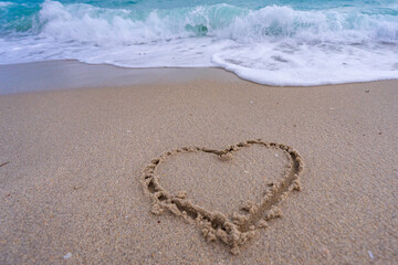 Heart drawn in sand. Waves forming a heart shape sign. Love on beach. Romantic summer. Heart made of sand. Love and ocean waves.