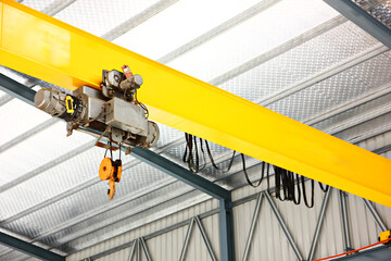 electric overhead crane install on yellow metal beam in warehouse. dictribution centers use cranes to move large quantities of heavy goods at once