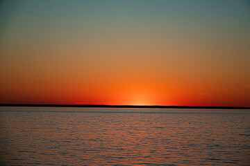 Vibrant colors fill the sky as the sun sets over tranquil waters, creating a peaceful atmosphere