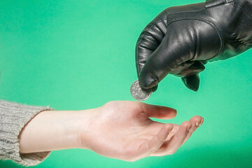 A large hand in a black glove holds a coin over a small hand.