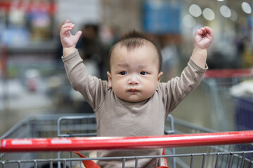Baby sitting in shopping cart at supermarket aisle