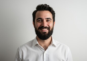Fototapeta premium Portrait of a smiling man with a beard wearing a white shirt against a plain white background
