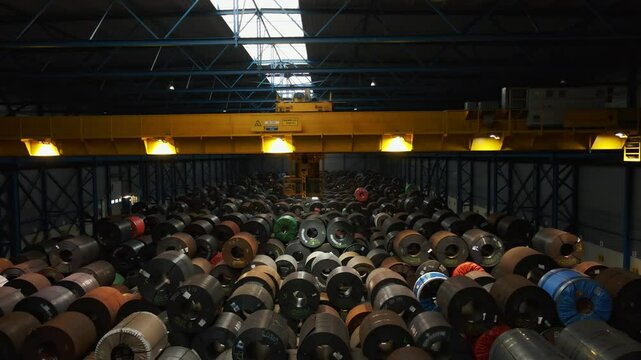 Large overhead bridge crane hanging in a large warehouse filled with steel coils