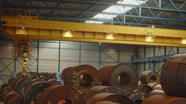 A large overhead Bridge Crane places a heavy steel coil in a large warehouse
