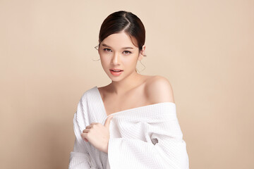 Obraz premium A beautiful young Asian woman with clean, fresh skin against a beige background. Skincare, facial treatment, cosmetology, beauty, and spa. An elegant portrait of an Asian woman.