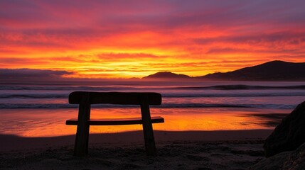 A wooden bench silhouetted by a vibrant and colorful sunset on a beach