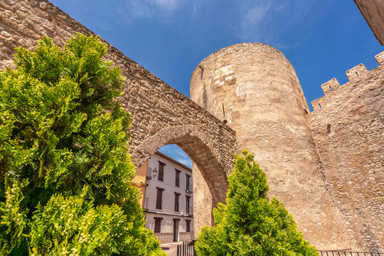 The Executioner&rsquo;s Tower stands beside a historic stone arch in the old town of Segorbe, Spain, framed by green trees and bathed in sunligh