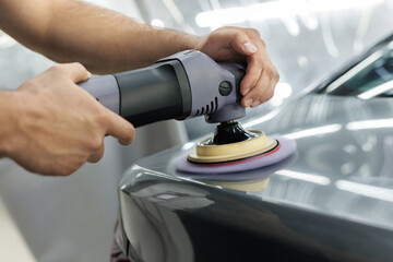 Car detailing - Man with orbital polisher in repair shop polishing car.