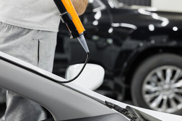 Worker applies special adhesive sealant to windscreen before installation on auto.