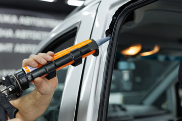 Worker applies special adhesive sealant to windscreen before installation on auto.