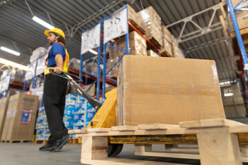 Fototapeta premium Close up cardboard crate, Man worker wear safety uniform push load cart goods to shelf in store. Company employees arrange products. Warehouse industrial stock storage.