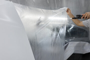 Detailer worker wets by spray PPF closeup. Car protection film apply.