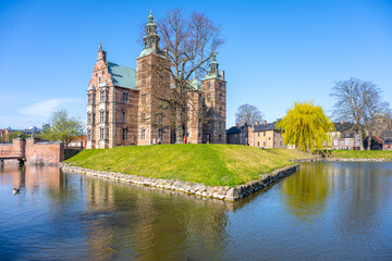 Obraz premium Rosenborg Castle stands majestically on its island surrounded by calm waters in Copenhagen. The clear blue sky enhances the castle's historic architecture, creating a picturesque view.