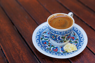 Traditional delicious Turkish coffee or Greek coffee with foam in ornate cup on wooden table