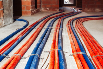 Workers are arranging red and blue pipes on the floor as part of the water communication setup for a bath complex under construction in a commercial building.